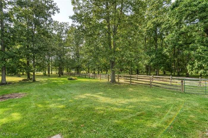 Open lawn bordered by mature trees and a wooden fence