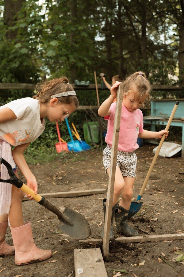 Two children digging in a raised garden bed with shovels